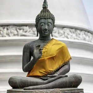 Bronze Buddha statue with yellow cloth in front of a white temple Bronze Buddha statue with yellow cloth in front of a white temple
