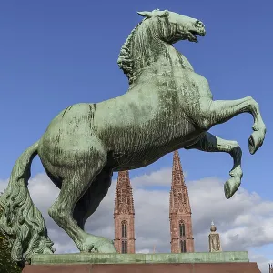 Bronze monument of a climbing horse in front of a neo-Gothic church Bronze monument of a climbing horse in front of a neo-Gothic church