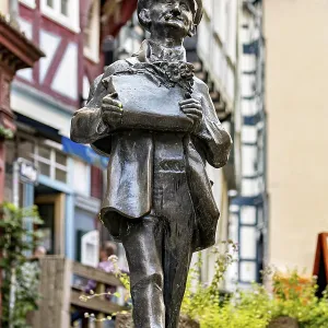 Bronze sculpture of a man with hat holding a card in a historic old town with half-timbered houses Bronze sculpture of a man with hat holding a card in a historic old town with half-timbered houses