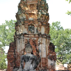 A Buddha statue seated before an ancient brick stupa