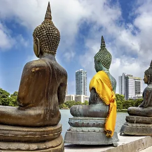 Buddha statues in bronze with yellow cloths in front of skyscrapers and water Buddha statues in bronze with yellow cloths in front of skyscrapers and water