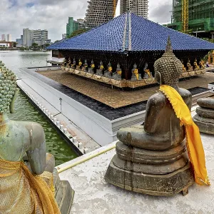 Buddha statues with yellow cloths sit in front of a modern cityscape on the water Buddha statues with yellow cloths sit in front of a modern cityscape on the water