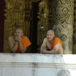 Buddhist monks leaning against a wall of Wat Mai Suwannaphumaham