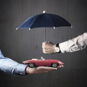 Businessman holding a small blue umbrella protecting a vintage car Businessman holding a small blue umbrella protecting a vintage car