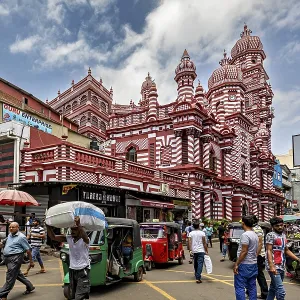 Bustling street scene with rickshaws and passers-by in front of a red architectural building