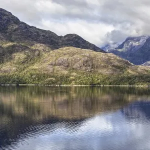 Calm ocean with clear reflection of forested mountains and cloudy skies in a peaceful setting
