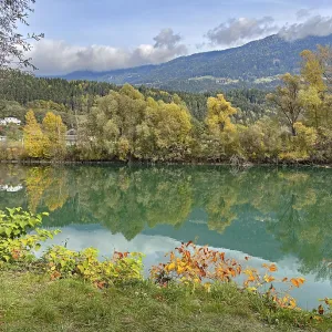 Calm river reflecting autumnal trees and mountains under cloudy sky