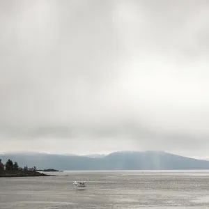 Calm water with distant mountains and a small float plane under an overcast sky in Nanaimo Calm water with distant mountains and a small float plane under an overcast sky in Nanaimo