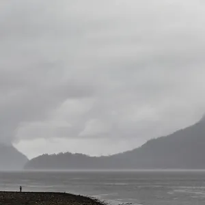 A calm waterscape with distant fog-covered mountains under heavy clouds along the lower mainland coast in British A calm waterscape with distant fog-covered mountains under heavy clouds along the lower mainland coast in British