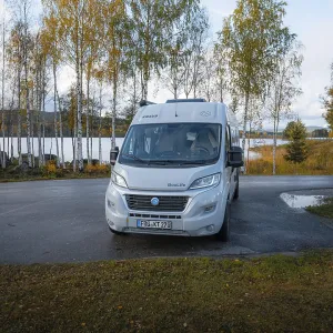 Campervan at resting place in front of autumn birch trees and lake