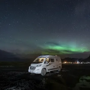 Campervan stands at Uttakleiv beach with northern lights