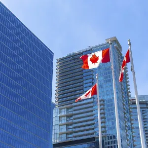 Three canadian flags are waving proudly against a backdrop of modern skyscrapers in downtown vancouver