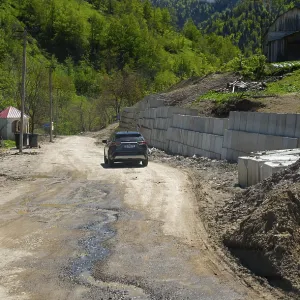 Car drives along a dirt road in a rural mountain landscape