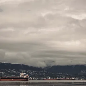 Cargo ships on the ocean with a mountainous backdrop under a cloudy sky Cargo ships on the ocean with a mountainous backdrop under a cloudy sky