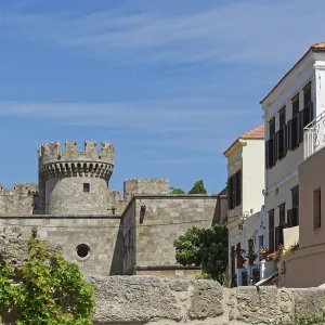 Castle with medieval stone towers next to a Mediterranean building under a blue sky