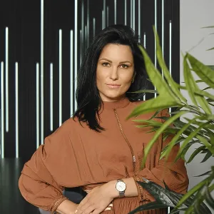 Casual lifestyle portrait of charming woman with black hair wearing brown dress posing near the potted plant