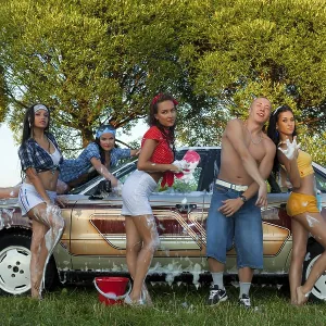 Cheerful female friends sitting on trunk of vintage car and looking at camera Cheerful female friends sitting on trunk of vintage car and looking at camera