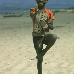 A cheerful local boy with a ripped shirt stands on the beach near Kande Beach on Lake Malawi and smiles at the camera A cheerful local boy with a ripped shirt stands on the beach near Kande Beach on Lake Malawi and smiles at the camera