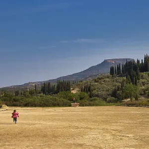 A child runs across a dry meadow to distant mountains