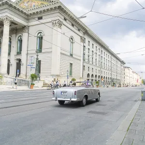 A classic car drives alongside a magnificent building in Munich