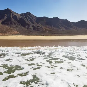 Clear beach with gentle waves against a mountain backdrop under a sunny sky Clear beach with gentle waves against a mountain backdrop under a sunny sky