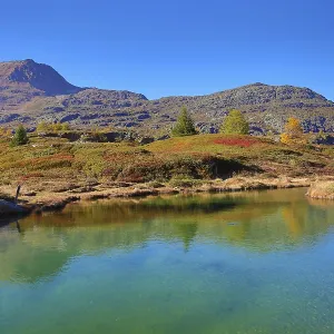 Clear reflections in a mountain lake with autumnal landscape and blue sky