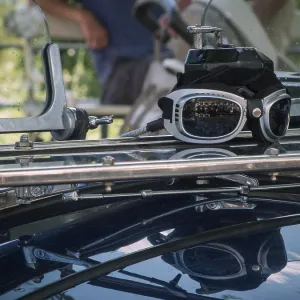 Close-up of a driver's goggles with reflection on the windscreen of a classic car against a blurred road