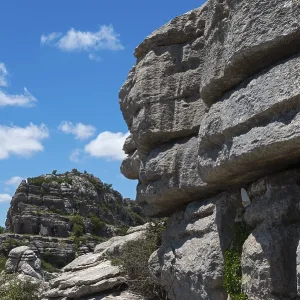Close-up of large rocks with blue sky and clouds in the background and green vegetation Close-up of large rocks with blue sky and clouds in the background and green vegetation