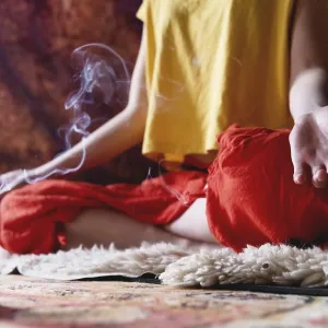 Close-up of woman's hand in yoga lotus pose meditating in a crafting room with candles<br> Close-up of woman's hand
