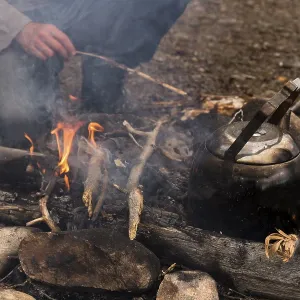 Coffee kettle on the campfire, behind it the legs of a person kneeling at the campfire Coffee kettle on the campfire, behind it the legs of a person kneeling at the campfire