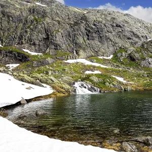 Cold summer in Norway. Large snowfields is reflected in the water of the lake