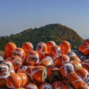 A collection of Daruma figures in front of a sun-drenched autumn landscape with mountains A collection of Daruma figures in front of a sun-drenched autumn landscape with mountains