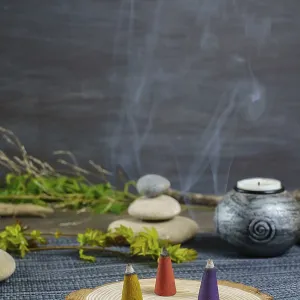 Colorful incense cones on a wooden disk with candles and zen stones stacked on top of them