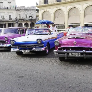 Several colorful vintage convertible cars park side by side on a busy street Several colorful vintage convertible cars park side by side on a busy street