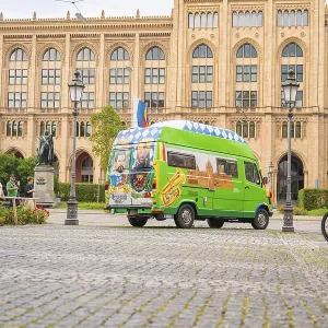 A colourfully painted bus in front of a historic building with a cobbled street and lanterns