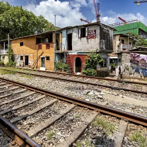 Construction cranes rise behind brightly painted houses along the train tracks under a blue sky