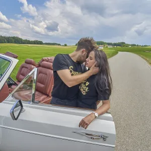 Couple sharing an affectionate moment by a white convertible on a rural road