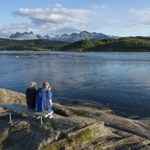 Couple sitting on a bench looking out to the tidal Saltstraumen strait in the evening light