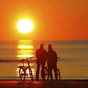Couples with bikes on the beach watching the sunset Couples with bikes on the beach watching the sunset