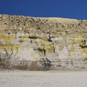 Crater wall with layers of yellow and beige rock under a blue sky Crater wall with layers of yellow and beige rock under a blue sky