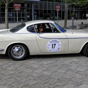 Cream-colored classic car with classic lines and drivers in an urban road environment