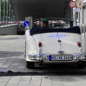 Cream-colored vintage cabriolet with number ND-XK140H in urban surroundings with street signs Cream-colored vintage cabriolet with number ND-XK140H in urban surroundings with street signs