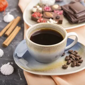 A cup of coffee with chocolate and coconut candies on a black concrete background and orange textile A cup of coffee with chocolate and coconut candies on a black concrete background and orange textile
