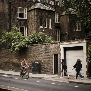 Cyclist and pedestrians pass a historic brick building on a cloudy day in Greater London Cyclist and pedestrians pass a historic brick building on a cloudy day in Greater London