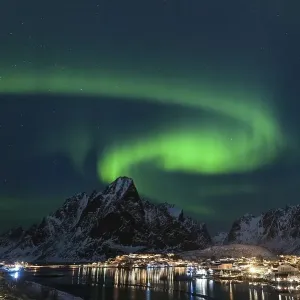 Dancing green polar lights over the village Reine on the Lofoten islands in Norway at night in winter with snow capped