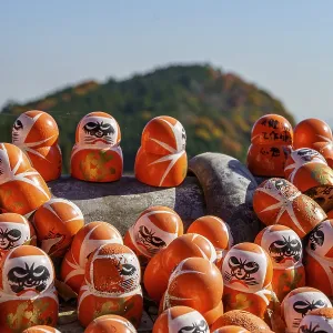 Several Daruma figures in front of an autumnal mountain and a blue sky Several Daruma figures in front of an autumnal mountain and a blue sky