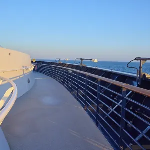 Deck of a cruise ship with clear blue sky and blue railing