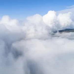 Dense clouds with mountains visible in the background under clear skies