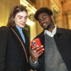 Diverse couple standing close, looking at a smartphone screen and smiling Diverse couple standing close, looking at a smartphone screen and smiling