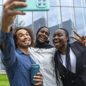 Three diverse friends smiling and laughing while taking a group selfie with a smartphone